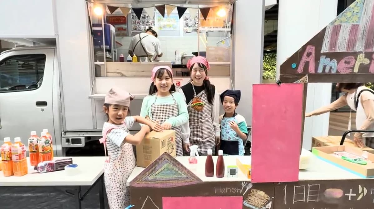 エプロン姿でパンケーキ店の前に立つ子どもたち